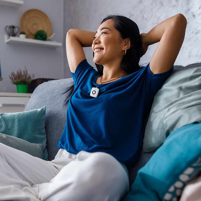 Woman wearing Mini Mobile System pendant sitting on couch