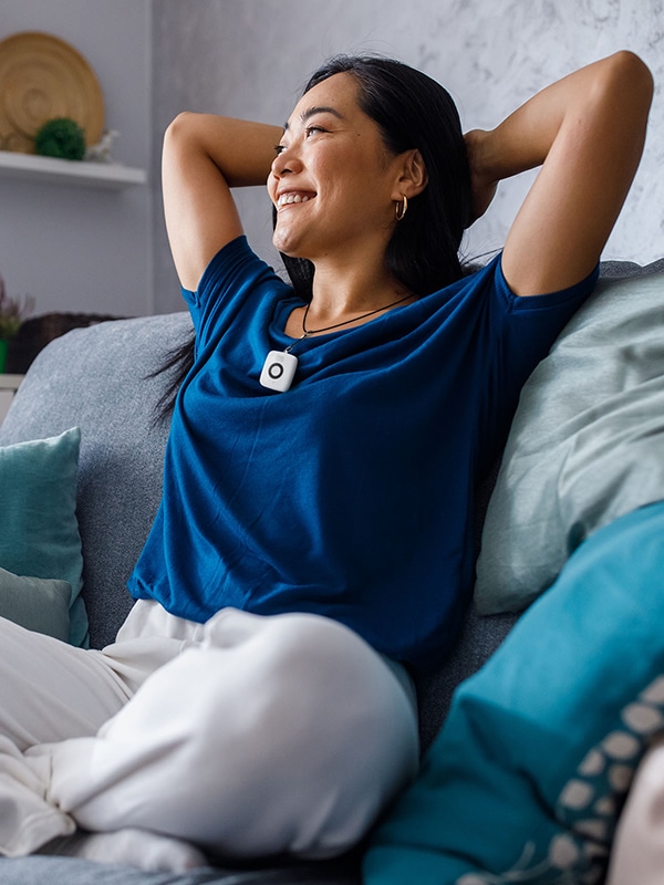 Woman wearing Medical Alert's Mini Mobile System pendant sitting on couch